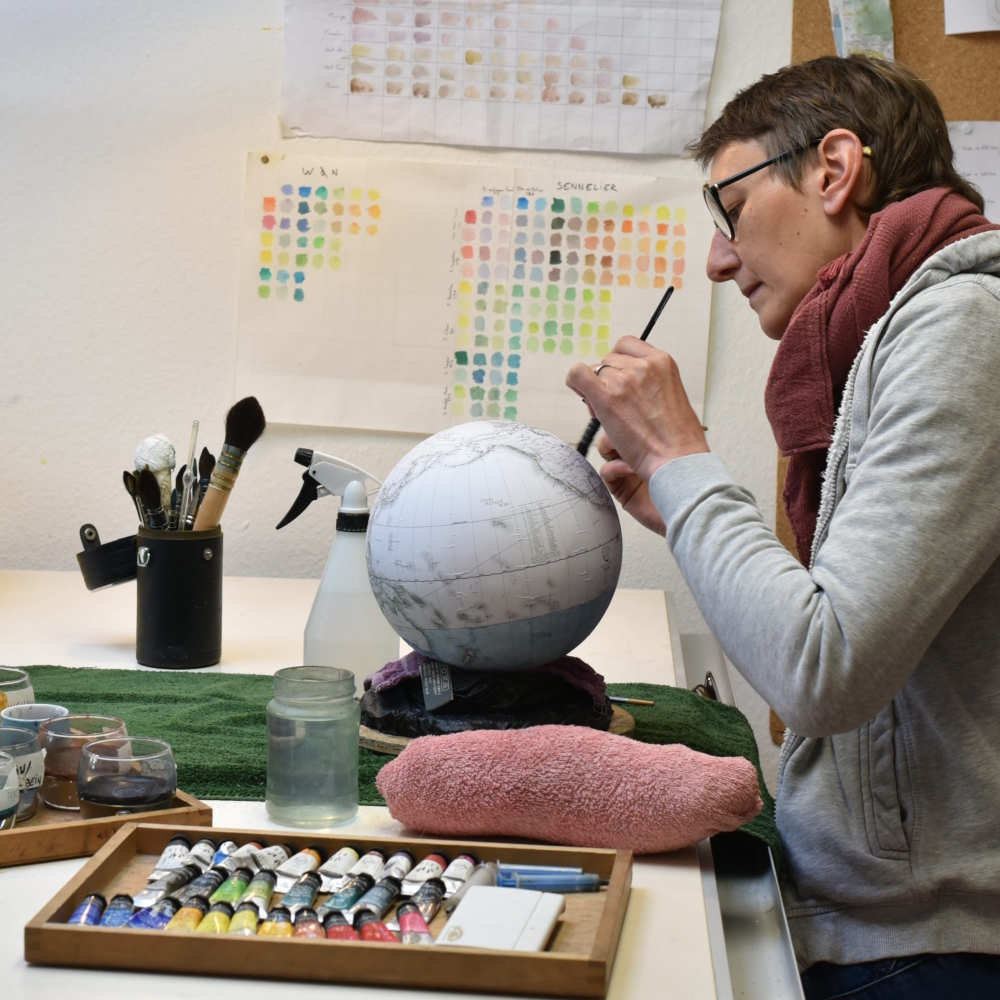 Cécile Blary does the finishing touches after having had hand colored the maps on each single globe.