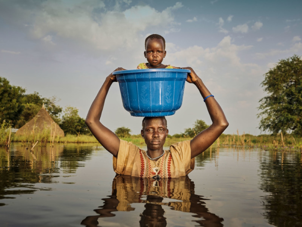 Nyalong Wal, 36, carries her daughter, Nyamal Tuoch, 2, to dry land in a bucket. Mothers do this to protect babies and children from falling into the deep floodwaters. (From 